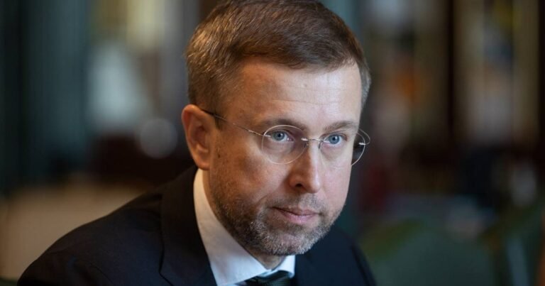 Прем'єр-міністр Сергій Корецький на тлі документів, що символізують законодавчі ініціативи уряду та бюджетний дефіцит.